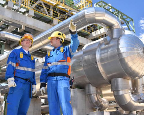 teamwork: group of industrial workers in a refinery - oil processing equipment and machinery